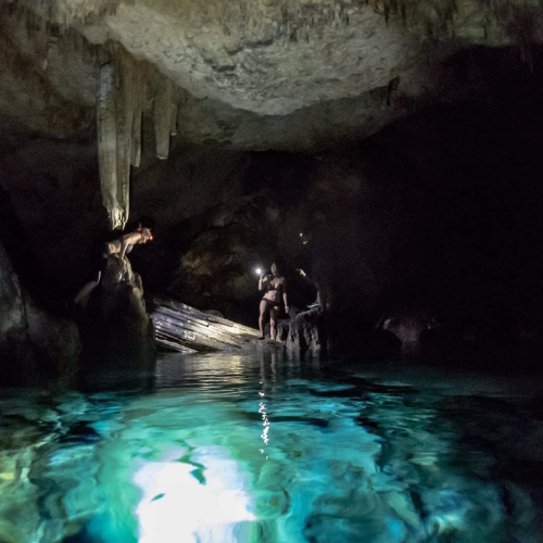 Inside a cave with a freshwater people lit up by underwater lights and one person about to jump in and another holding the flashlight, Gorgeous blue water